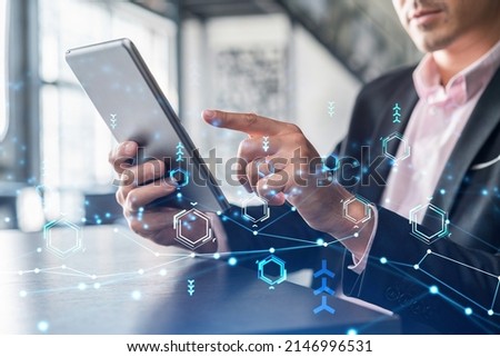 Businessman in suit using tablet device to optimize development by implying new technologies in business process. Interconnections and hi tech hologram over modern panoramic office background