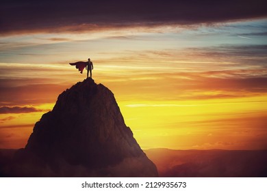 Businessman superhero conceptual scene. Determined hero with red cape stands brave on a mountain peak. Business leadership, ambition and strength metaphor. Overcome obstacles and achieve success - Powered by Shutterstock