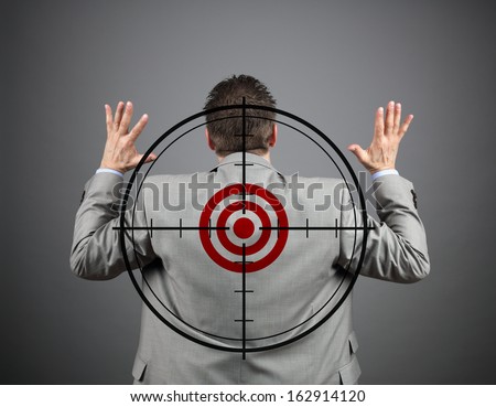 Businessman surrendering with crosshair and target on his back