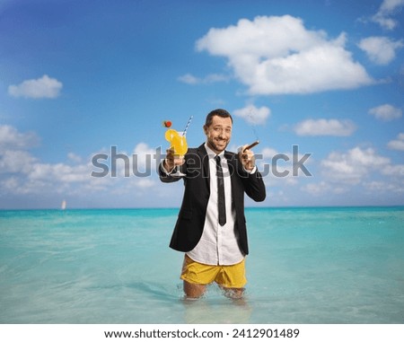 Businessman in swimming shorts with a cocktail and a cigar standing in the Caribbean sea