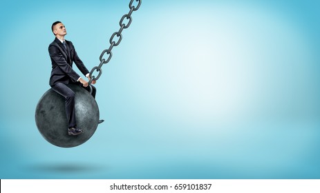 A businessman swinging on a large wrecking ball and looking up on blue background. Harness your problems. Stepping stones and challenges. Right motivation.