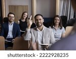 Businessman take part in educational, motivational training event seated with colleagues attend together in seminar, raises his arm for ask question, participate in voting, having opinion to share it