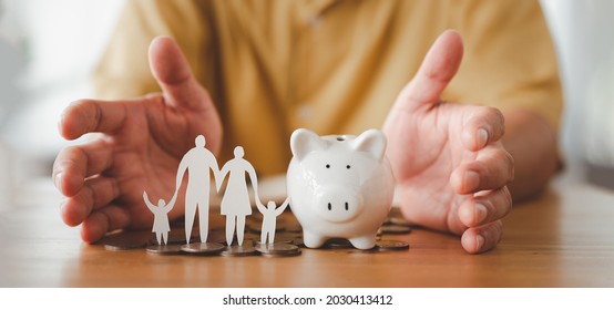 Businessman take a position to protect on the piggybank and paper family in hand, donation, saving, charity, family finance plan concept, fundraising, superannuation, financial crisis concept