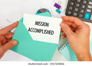 The businessman takes out a card from the envelope with the text Mission Accomplished, on the background of the office desk. - Shutterstock ID 1917235856