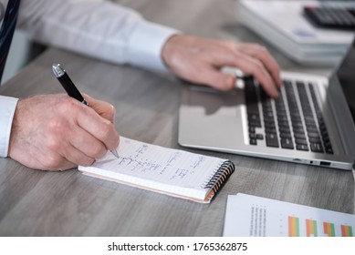 Businessman taking notes while using laptop