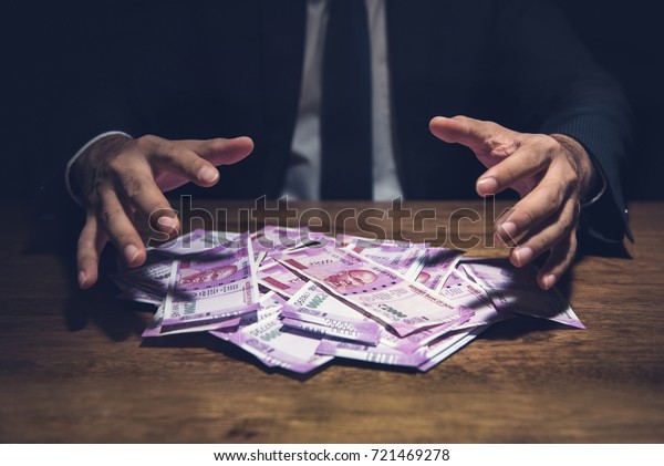 Businessman taking pile of\
money, Indian Rupee banknotes, on his desk in a dark office  -\
corruption concept