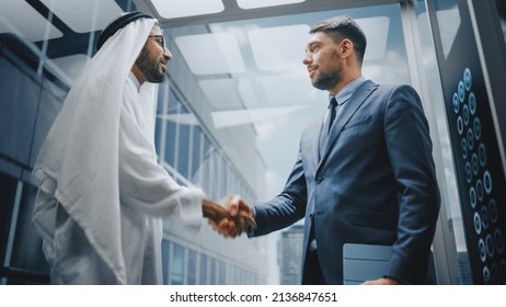 Businessman Talking with Arab Investment Partner while Riding Glass Elevator to Office in a Modern Business Center. International Corporate Associates Shake Hands and Agree on a Deal in a Lift. - Powered by Shutterstock