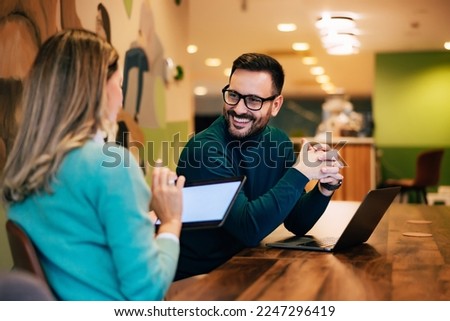 Businessman talking with a female colleague about their accomplishments, sitting at the office.