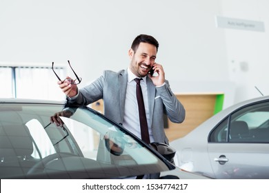 Businessman Talking On Phone Near Car In Modern Dealership.