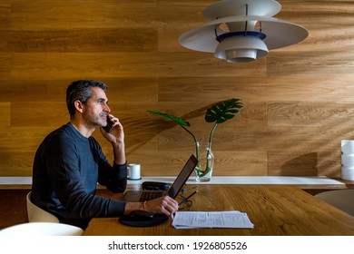 Businessman Talking On The Phone And Working On His Laptop In His Living Room