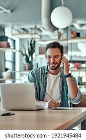 Businessman Talking On Smartphone In Cafe. Casual Man Making Notes While Working On Laptop Computer At Remote Workplace