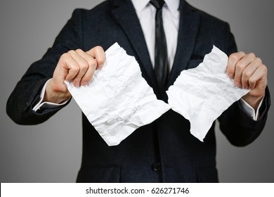 Businessman tearing hands crumpled sheet of A4 paper. Isolated on grey background.
