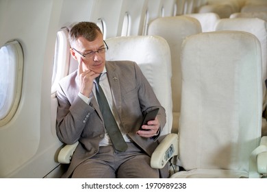 Businessman thinking and checking mobile phone in first class seat by airway travel flight - Powered by Shutterstock