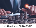 Businessman touch arrow showing financial growth 2023 on stacked coins business background,Concepts savings money and accounting, investments, banks, bonds, dividends, inflation and digital assets.  