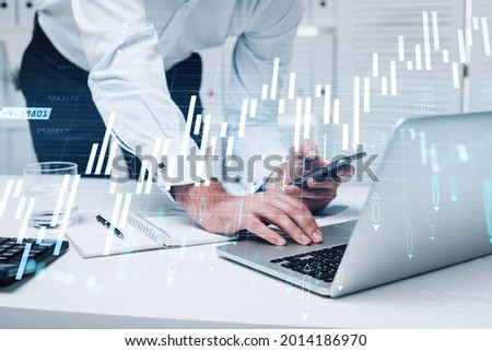 Businessman trader is using laptop to continue trading operations and checking quotes in smartphone. Office background. Concept of analyzing stock market behavior. Successful growth of the income