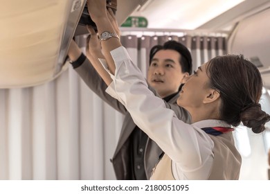 Businessman traveller putting luggage in overhead compartments with female flight attendant helping, cabin crew woman working on board, female airhostess helping passenger put suitcase in compartment