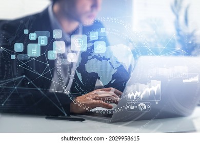 Businessman is typing message on laptop with digital interface with globe, cloud data, padlock, coin icons. Office workplace in the background. Concept of international business and communication