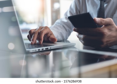 Businessman Typing On Laptop Computer Keyboard And Using Mobile Smart Phone With Digital Tablet On Desk. Business Man Connecting Internet, Networking In Modern Office, Closeup