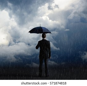 Businessman with umbrella standing over stormy background. Business, protection, crisis concept.   - Powered by Shutterstock