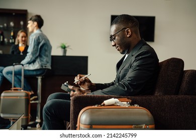 Businessman Uses Smartphone Waiting For A Flight, Traveling Entrepreneur Remote Work Online Sitting In A Boarding Lounge Of Airline Hub.