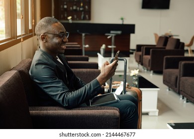 Businessman Uses Smartphone Waiting For A Flight, Traveling Entrepreneur Remote Work Online Sitting In A Boarding Lounge Of Airline Hub.