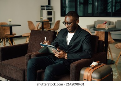 Businessman Uses Tablet Waiting For A Flight, Traveling Entrepreneur Remote Work Online Sitting In A Boarding Lounge Of Airline Hub.