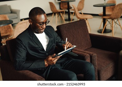 Businessman Uses Tablet Waiting For A Flight, Traveling Entrepreneur Remote Work Online Sitting In A Boarding Lounge Of Airline Hub.