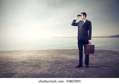 Businessman using binoculars with seascape in the background - Powered by Shutterstock