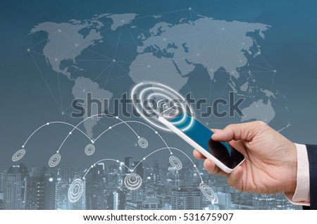 Businessman using blue screen mobile smartphone and city night in blue tone background with digital alarm wifi icon, internet of things IOT, smart city concept