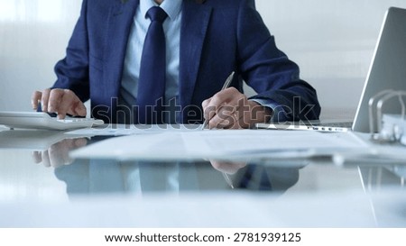 Businessman using calculator and taking notes, working with laptop and documents at office desk. Audit and taxes theme in business