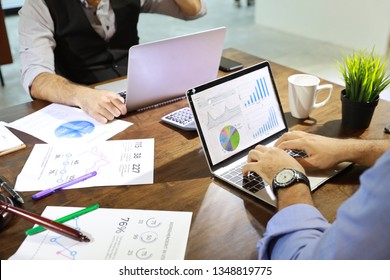 businessman using computer with chart on screen and company graph summary report on table with coffee cup and calculator beside