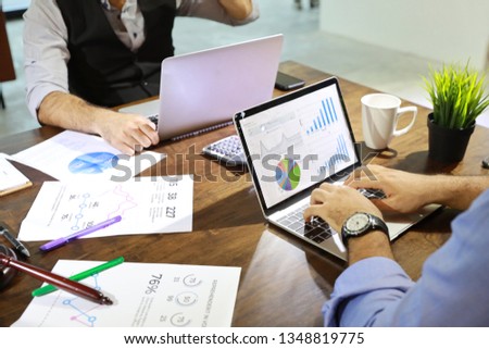 businessman using computer with chart on screen and company graph summary report on table with coffee cup and calculator beside