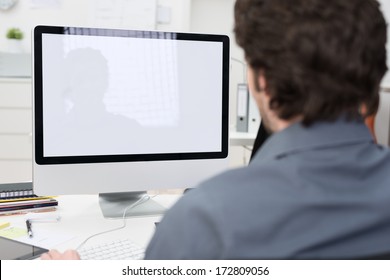 Businessman using a desktop computer with a view over his shoulder from behind of the blank screen of the monitor
