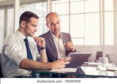 Businessman Using A Digital Tablet To Discuss Information With Senior Leadership In A Meeting. Business Partners Discussing Plans. Mature Boss And Young Business Man Working Together In Office.