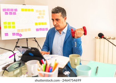 businessman using dumbbells weigth in office working - successful business man holding a heavy dumbbell - Executive exercising doing weights and working at office - Businessman in office exercising  - Powered by Shutterstock