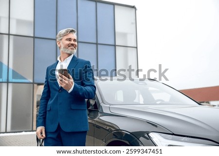 Businessman using his smartphone while standing at dealership