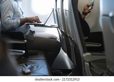 Businessman Using Laptop In Airplane And Passenger In Front Row With Cellphone. Airline Wifi Connection, Device Flight Mode Concepts