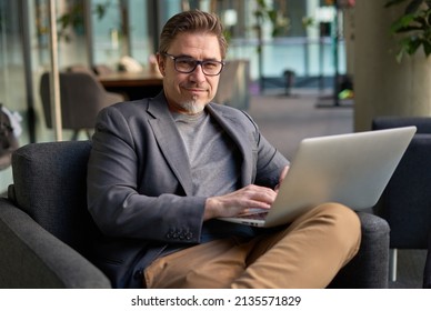 Businessman Using Laptop Computer In Office Lobby Or On Cafe Terrace. Happy Middle Aged Man, Entrepreneur, Small Business Owner Working Online.