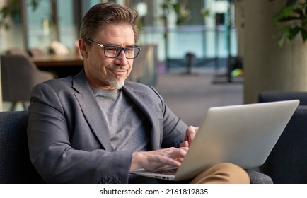 Businessman Using Laptop Computer In Office Lobby Or On Cafe Terrace. Happy Middle Aged Man, Entrepreneur, Small Business Owner Working Online.