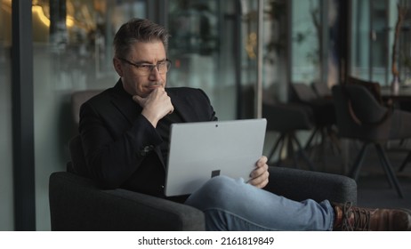 Businessman Using Laptop Computer In Office Lobby Or On Cafe Terrace. Happy Middle Aged Man, Entrepreneur, Small Business Owner Working Online.