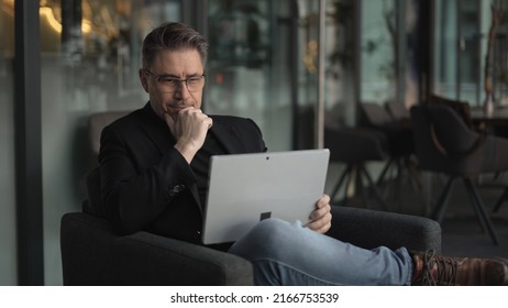 Businessman Using Laptop Computer In Office Lobby Or On Cafe Terrace. Happy Middle Aged Man, Entrepreneur, Small Business Owner Working Online.