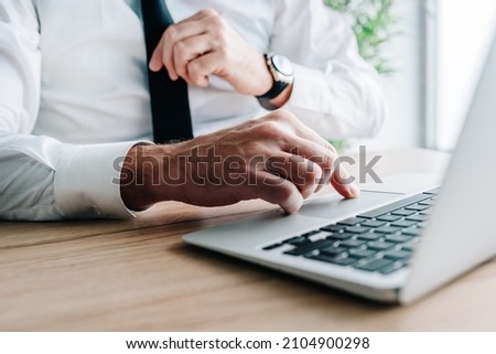 Businessman using laptop computer at office desk, hand on a trackpad or touchpad, selective focus