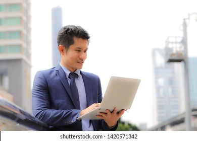 Businessman using laptop computer outdoors in the city - mobile business, working anywhere concepts. Close-up of businessman in stylish blue suit using modern laptop on city background. - Shutterstock ID 1420571342