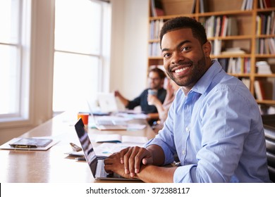 Businessman Using Laptop At Desk In Busy Office