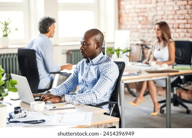 Businessman using laptop at desk in office with colleagues in background