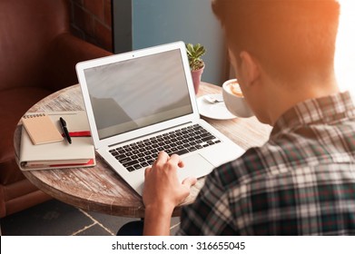 Businessman using laptop with tablet and pen on wooden table in coffee shop with a cup of coffee