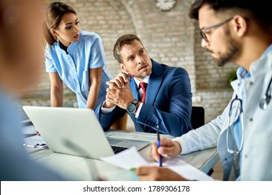 Businessman Using Laptop While Communicating With Healthcare Workers During The Meeting In The Office. 