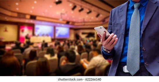 businessman using the mobile phone, blurred of conference hall or seminar room with attendee background. - Powered by Shutterstock