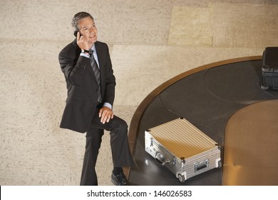 Businessman Using Mobile Phone By Luggage On Carousel In Airport