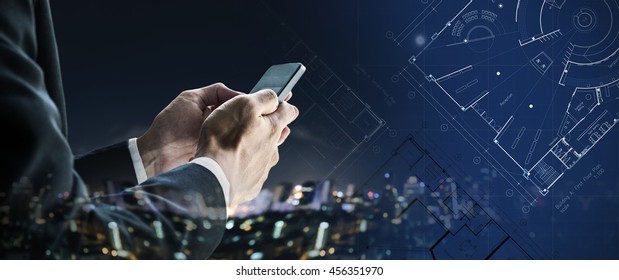 Businessman using mobile phone with city at night and blueprint architectural drawing plan 